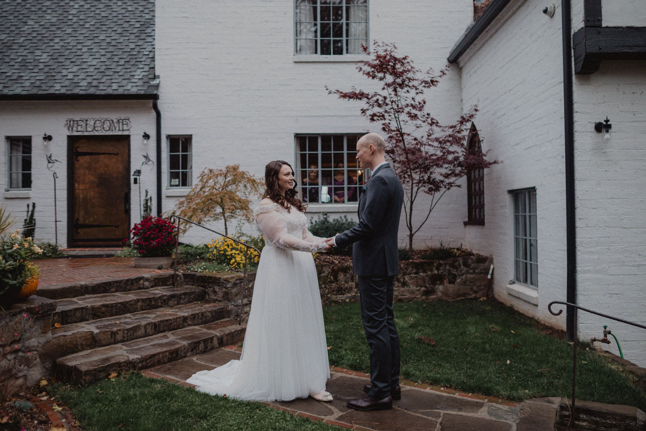 A couple shares an intimate moment during their wedding ceremony outside a white house with stone steps.