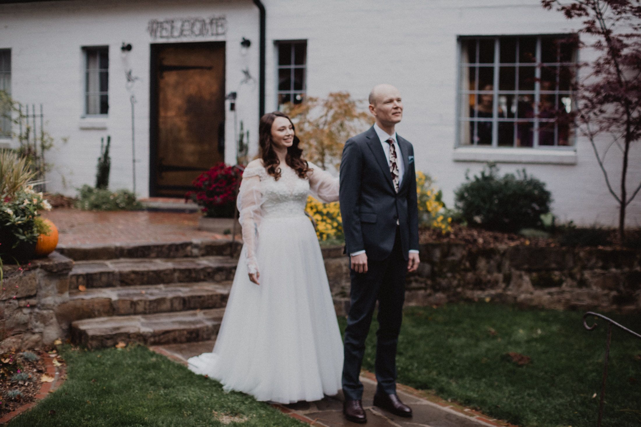 A romantic wedding photo series showing a couple walking together outside a white building with fall decorations.