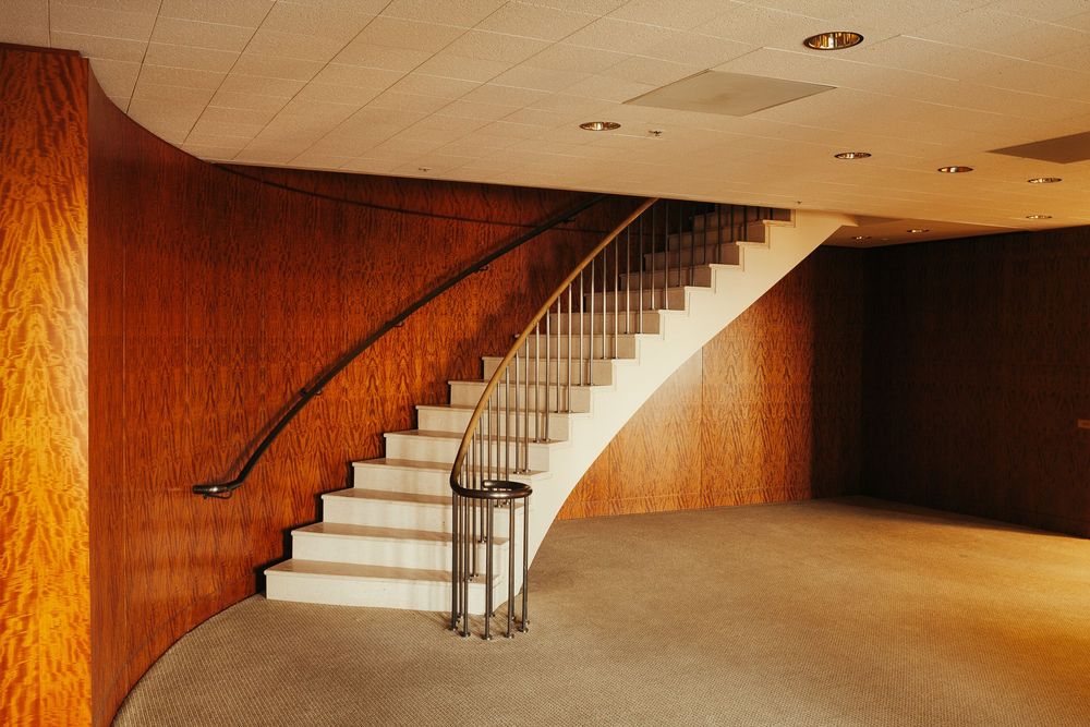 Curved staircase with wood paneling and metal railings in a minimalist interior space.