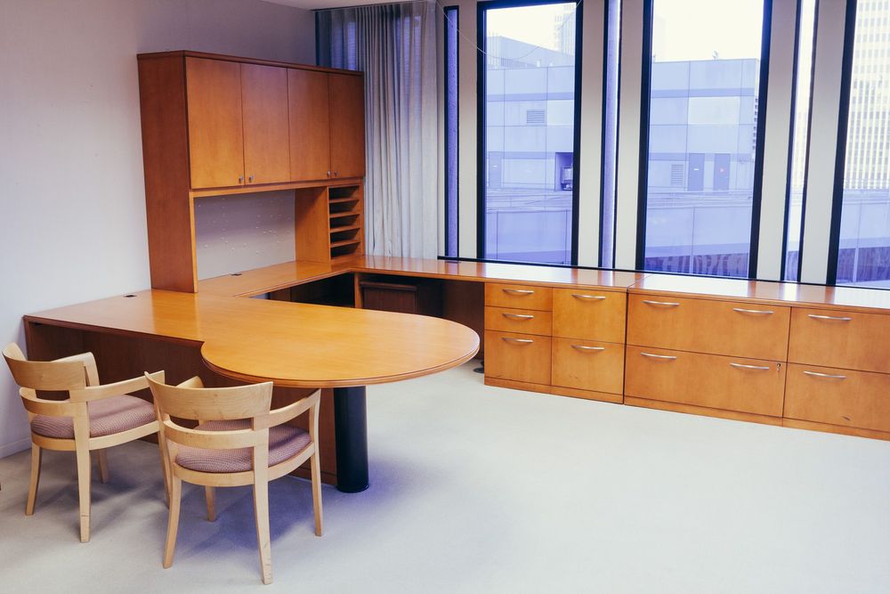 Modern office space with wooden furniture and large windows providing natural light.