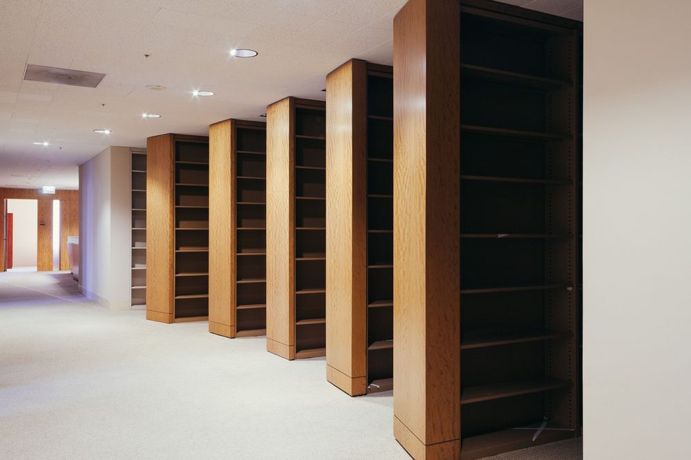 Long corridor with alternating wooden pillars and dark shelving units along one wall.