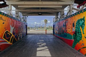 Covered walkway with vibrant graffiti murals on both walls leading to beach view.