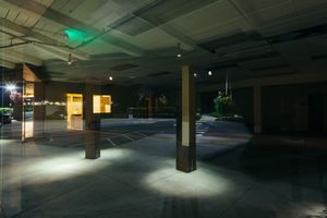 Dimly lit parking garage interior with spotlights creating dramatic shadows.