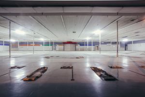 Large empty commercial space with fluorescent lighting and suspended ceiling tiles.