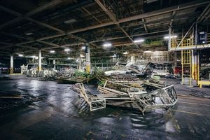 Abandoned warehouse interior with scattered debris and damaged equipment on wet floor.
