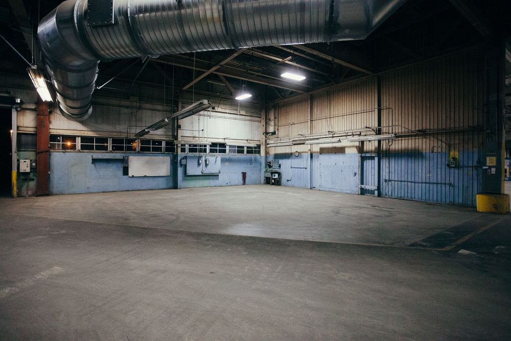 Large empty industrial warehouse interior with concrete floor and metal ceiling.