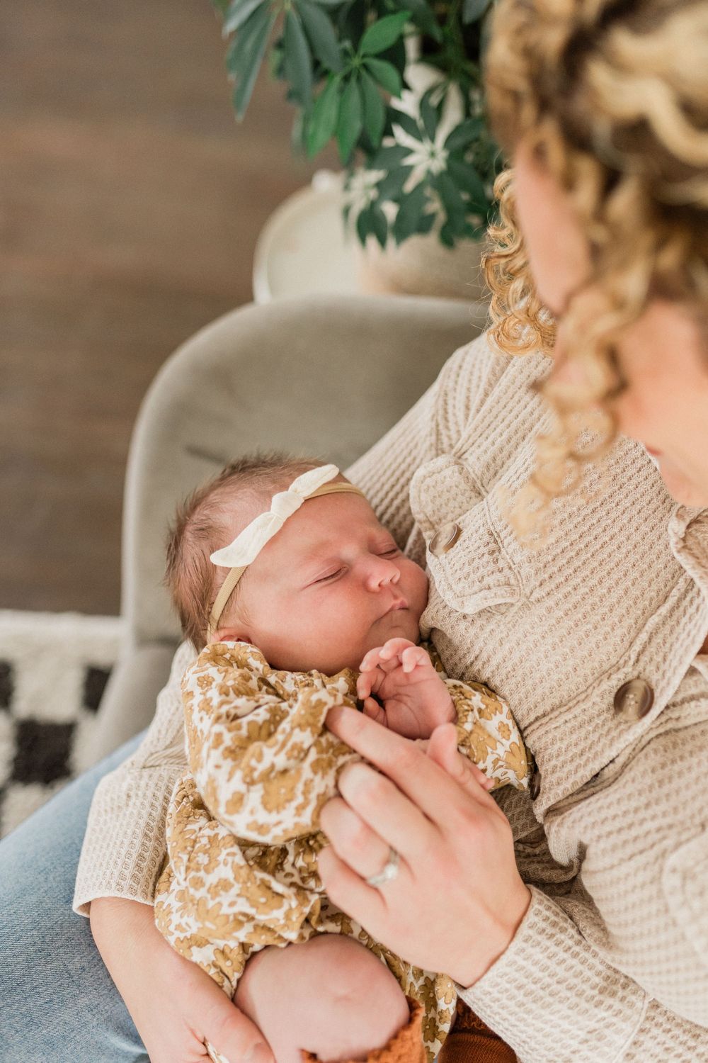 A sleeping newborn baby wearing a floral outfit is cradled in someone's arms wearing a cream knit sweater.
