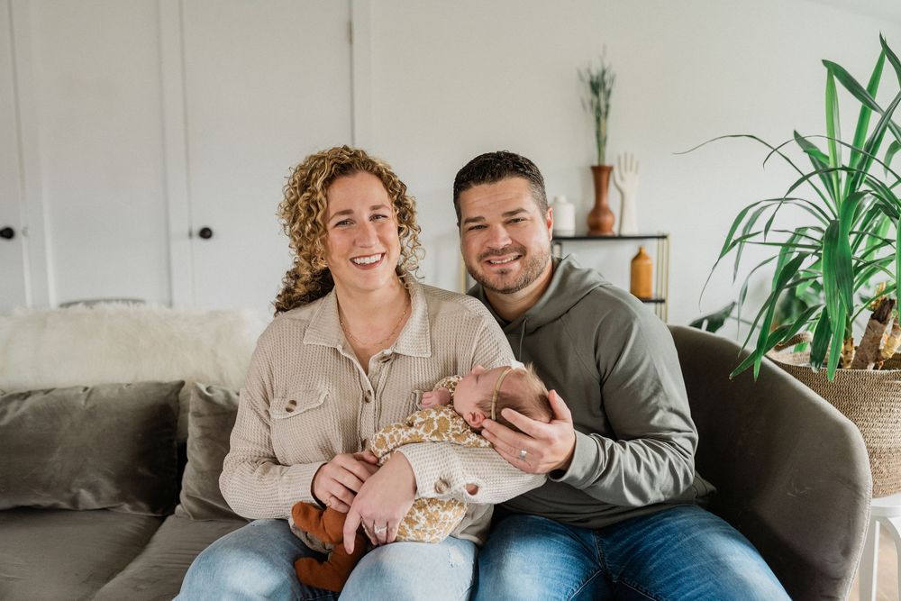 A couple laughs together while relaxing on a grey couch in a bright, modern living room with houseplants.