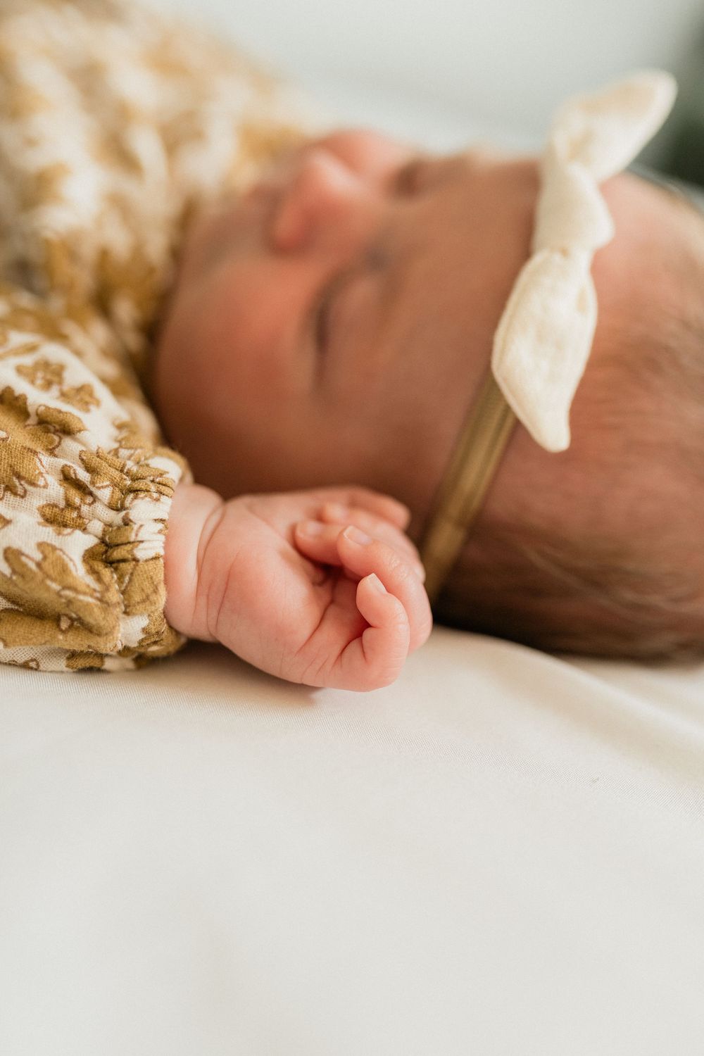 Close-up details of a sleeping newborn baby's tiny hands and floral outfit against a white background.