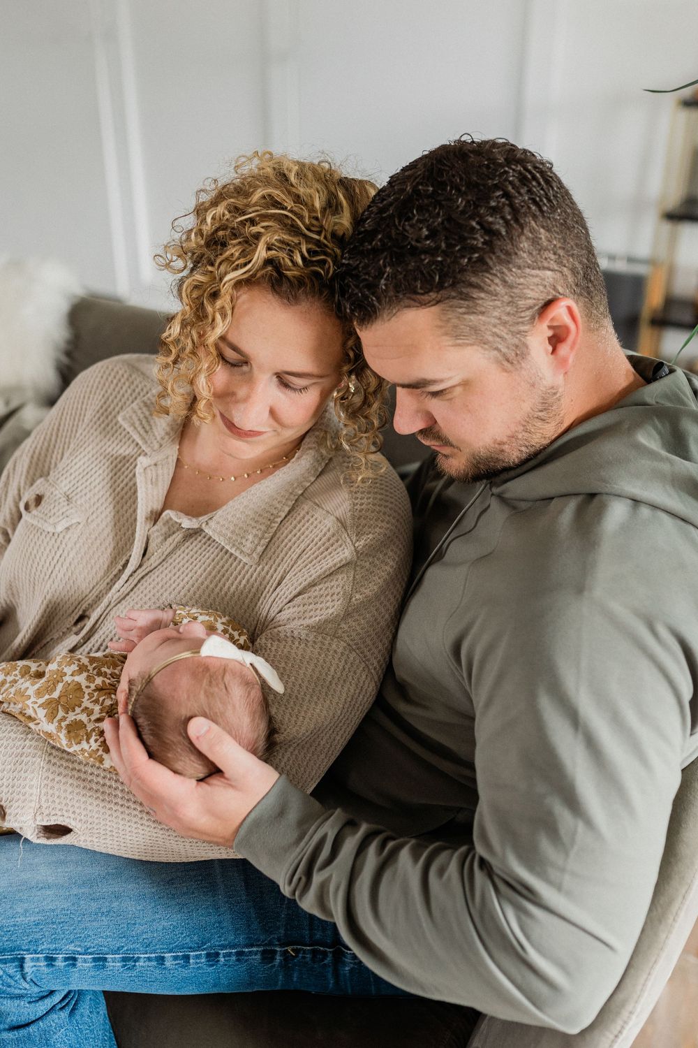 Parents share intimate bonding moments with their infant while relaxing on a gray couch.