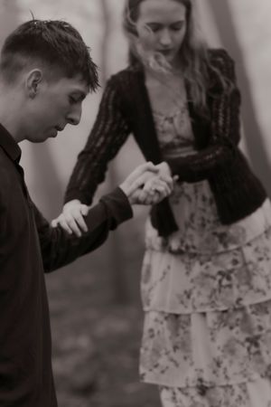 Black and white photo of a young couple holding hands outdoors, woman in floral dress and cardigan.