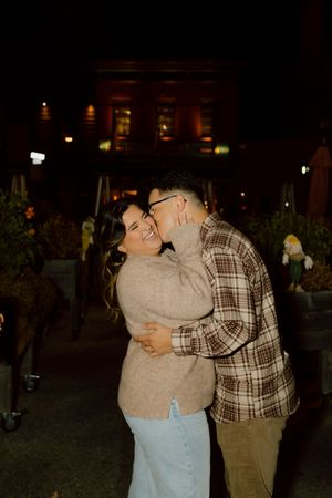 Couple embracing and laughing together outside at night near a warmly lit brick building.