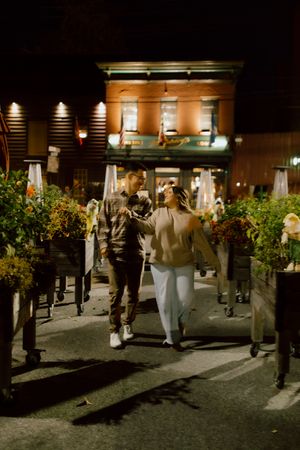 Couple walking hand-in-hand through a romantic outdoor restaurant patio at night with warm glowing lights.