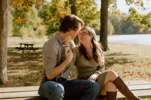 Romantic couple sharing a close moment while sitting on a park bench with autumn trees nearby.