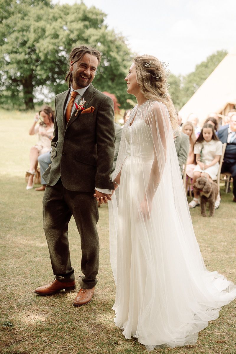 A couple shares a joyful ceremony moment at an outdoor wedding at tipis riley green, with the bride's flowing white dress swaying in motion.