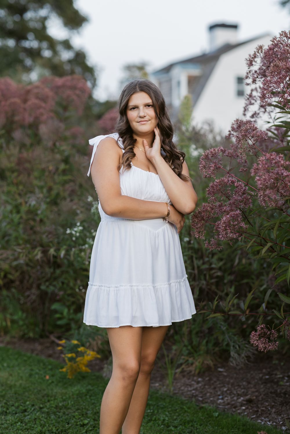 A senior girl with long brown hair wears a white dress for senior photos at Stevens Coolidge Estate in North Andover, MA for senior photos.