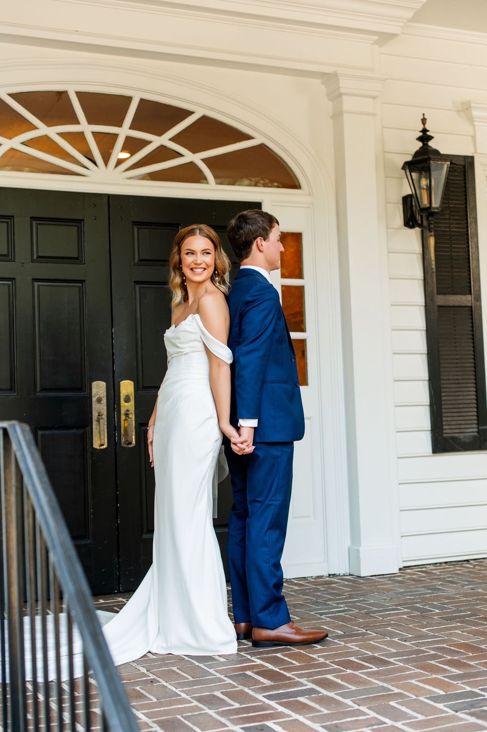 A bride and groom share a moment on their wedding day in front of a white colonial entrance.