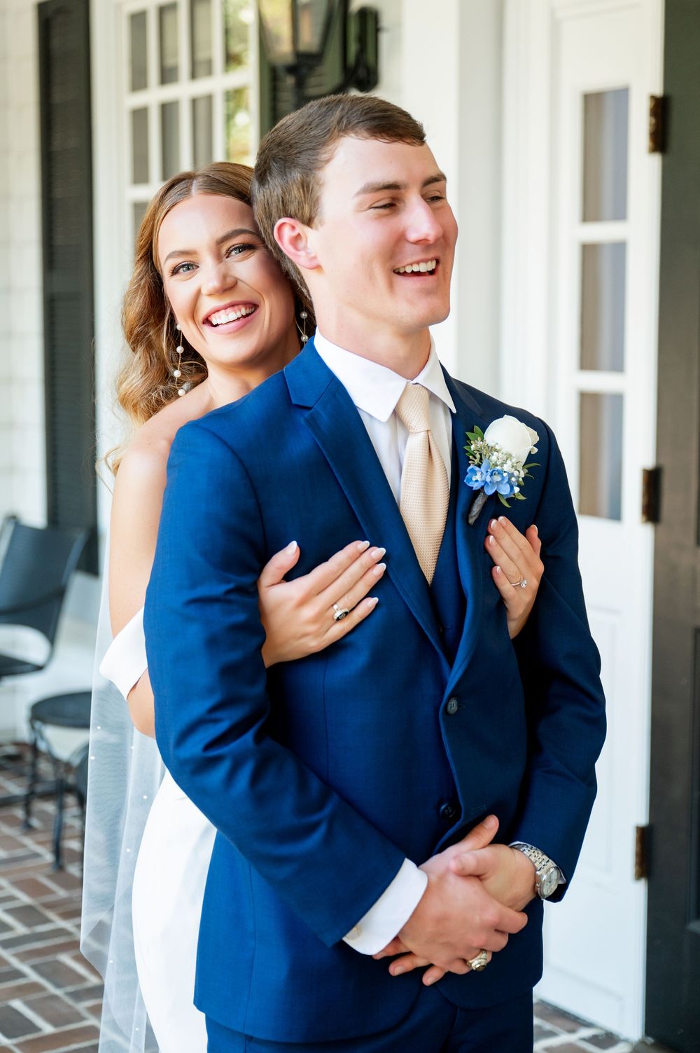 Candid moments of a couple laughing together during their first look on a white porch.