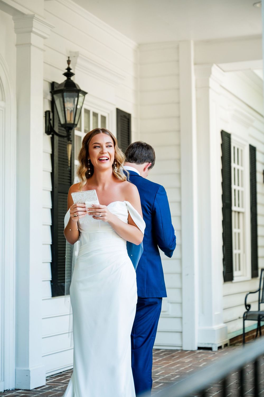 A couple shares a joyful first look moment on a white columned porch during their wedding day.