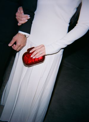 A close-up of hands holding a red clutch purse against a white flowy dress.