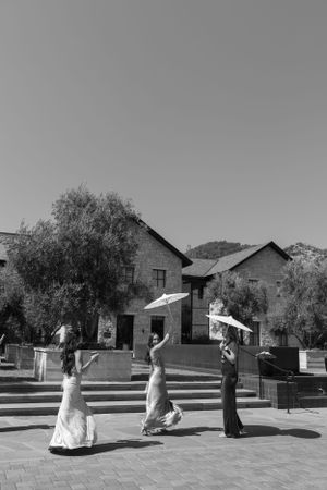Three figures dancing with parasols in black and white against stone buildings.