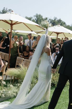 Outdoor wedding ceremony with guests under white umbrellas surrounded by natural landscaping.