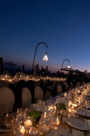 Romantic dinner table setup with glowing candles and hanging lanterns against a deep blue twilight sky.