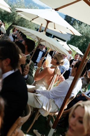 Outdoor wedding celebration with guests gathering under white umbrellas on a sunny day.