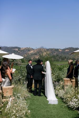 Outdoor wedding ceremony with mountain backdrop and white parasols lining the aisle.