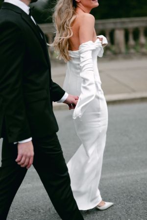Close up of bride in fitted white gown walking with groom in classic tuxedo.