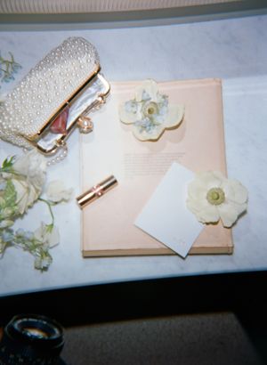 Wedding accessories including a clutch and floral decorations arranged on a pink surface.