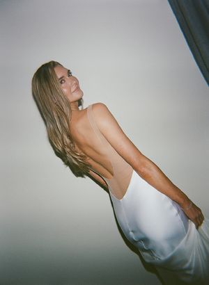 A portrait of a person in a white dress posing against a plain backdrop in an artistic fashion photograph.