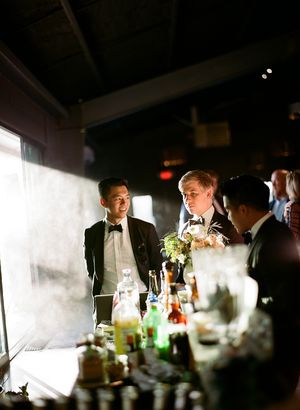 Wedding reception guests gathered at a dimly lit bar with bottles and glassware.