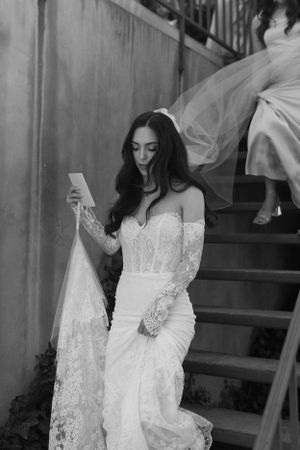 Figure in lace wedding dress reading on staircase.