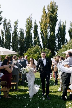Wedding ceremony recessional on grass lawn with tall trees in background.