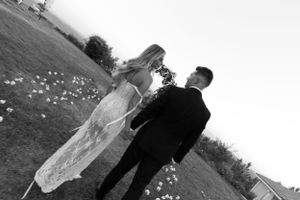 Black and white wedding photo of a couple walking through scattered flower petals on a lawn.