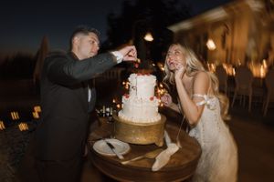Playful cake cutting moment captured during outdoor evening wedding reception.