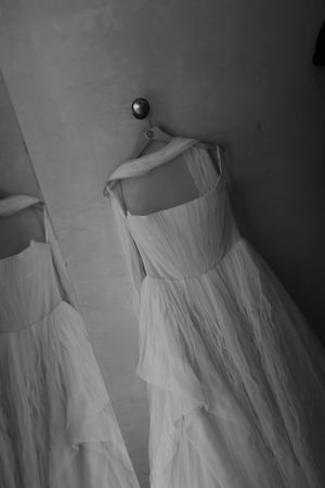 A black and white photograph of delicate white vintage dresses hanging on a wall, with romantic flowing fabric details.