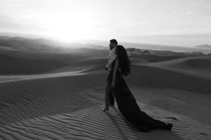 Dramatic silhouette of figure walking across desert sand dunes at sunset.