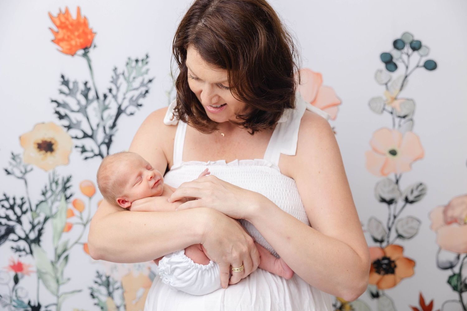 A tender moment between mother and newborn baby against a floral wallpaper background.