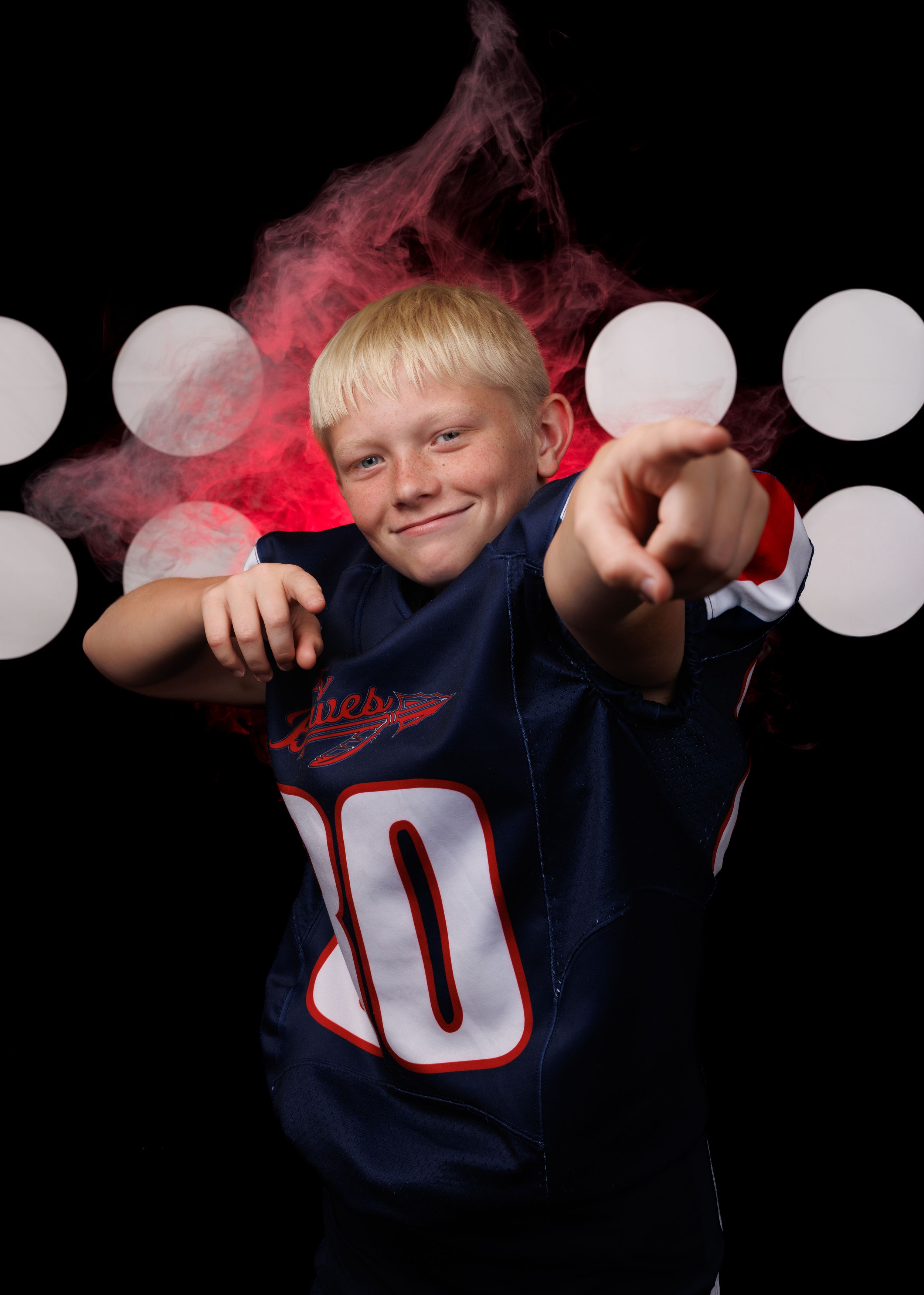 Youth athlete in navy blue jersey poses dramatically with red lighting effects.