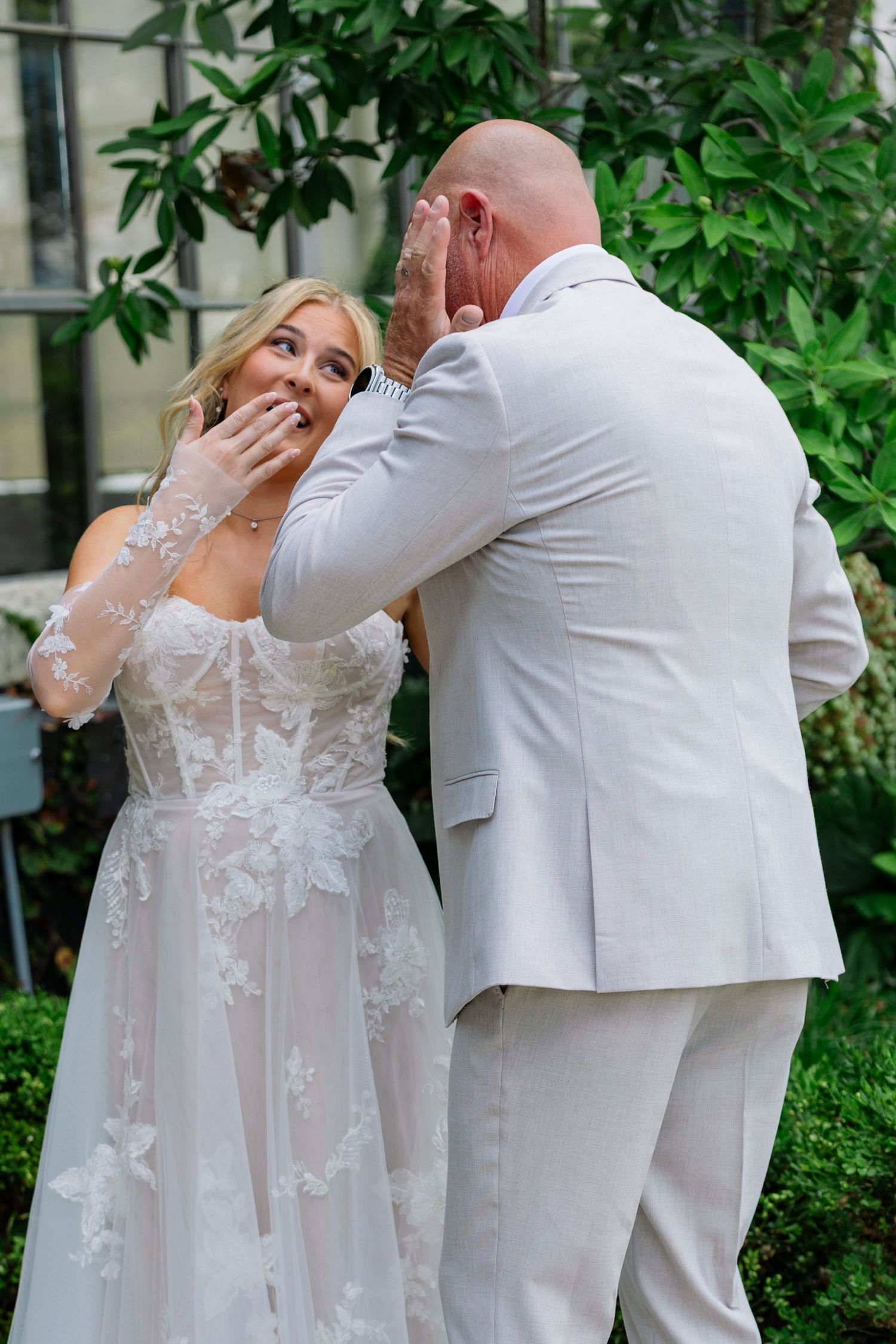 A wedding couple shares their first look moment in a garden setting wearing elegant white attire.
