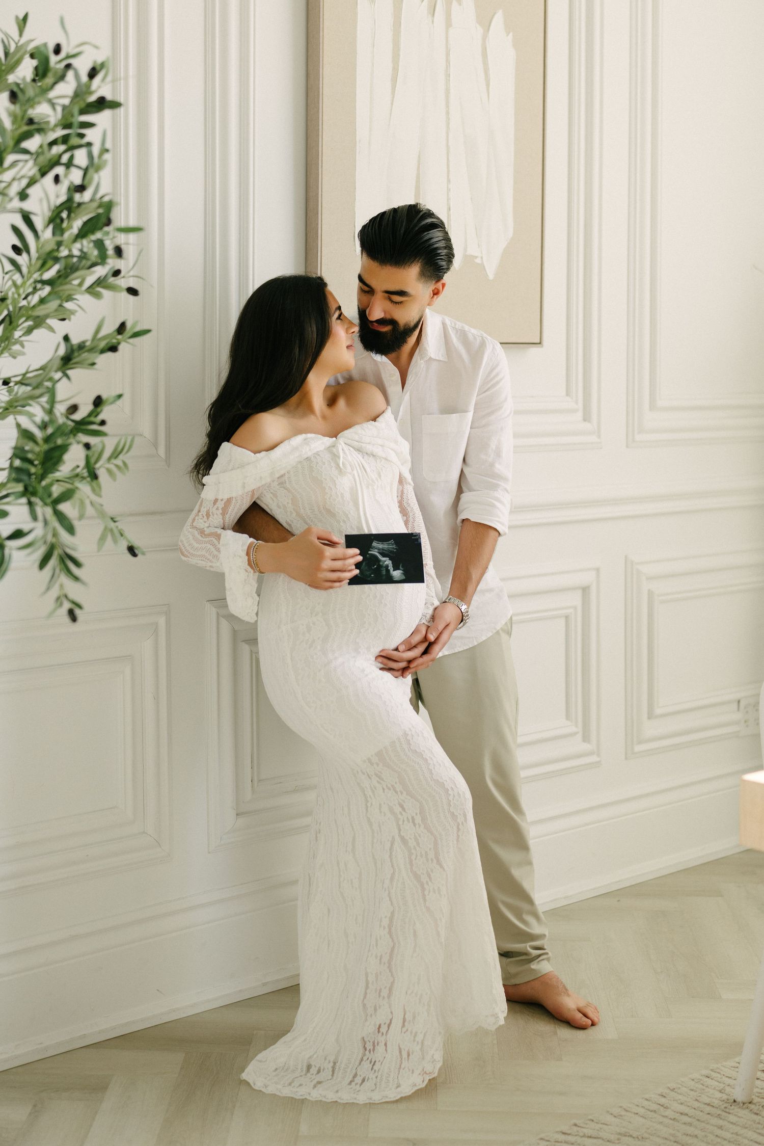 Expectant couple embracing in a bright studio with panelled walls.