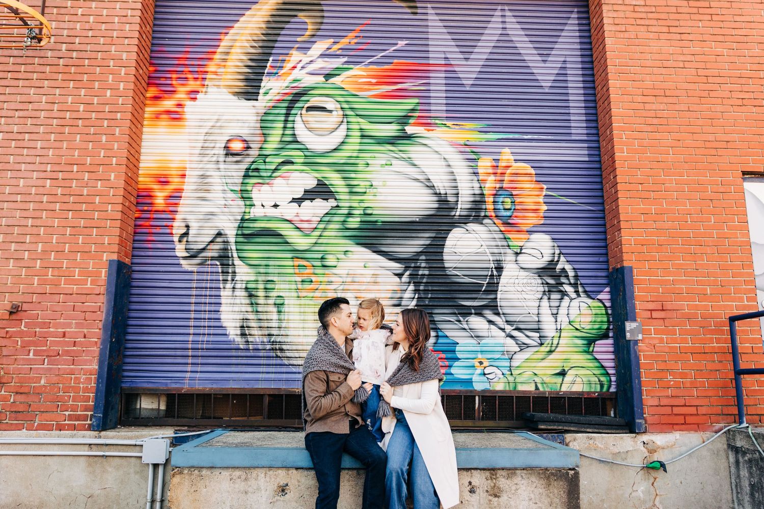 A family poses against a colorful graffiti wall with vibrant street art in an urban setting for Charlotte family photos.