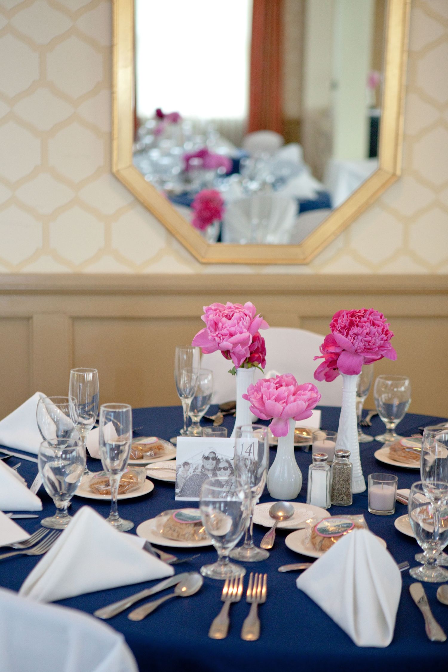 Elegant table setting with navy blue linens, white napkins, and bright pink peony centerpieces for a formal event.