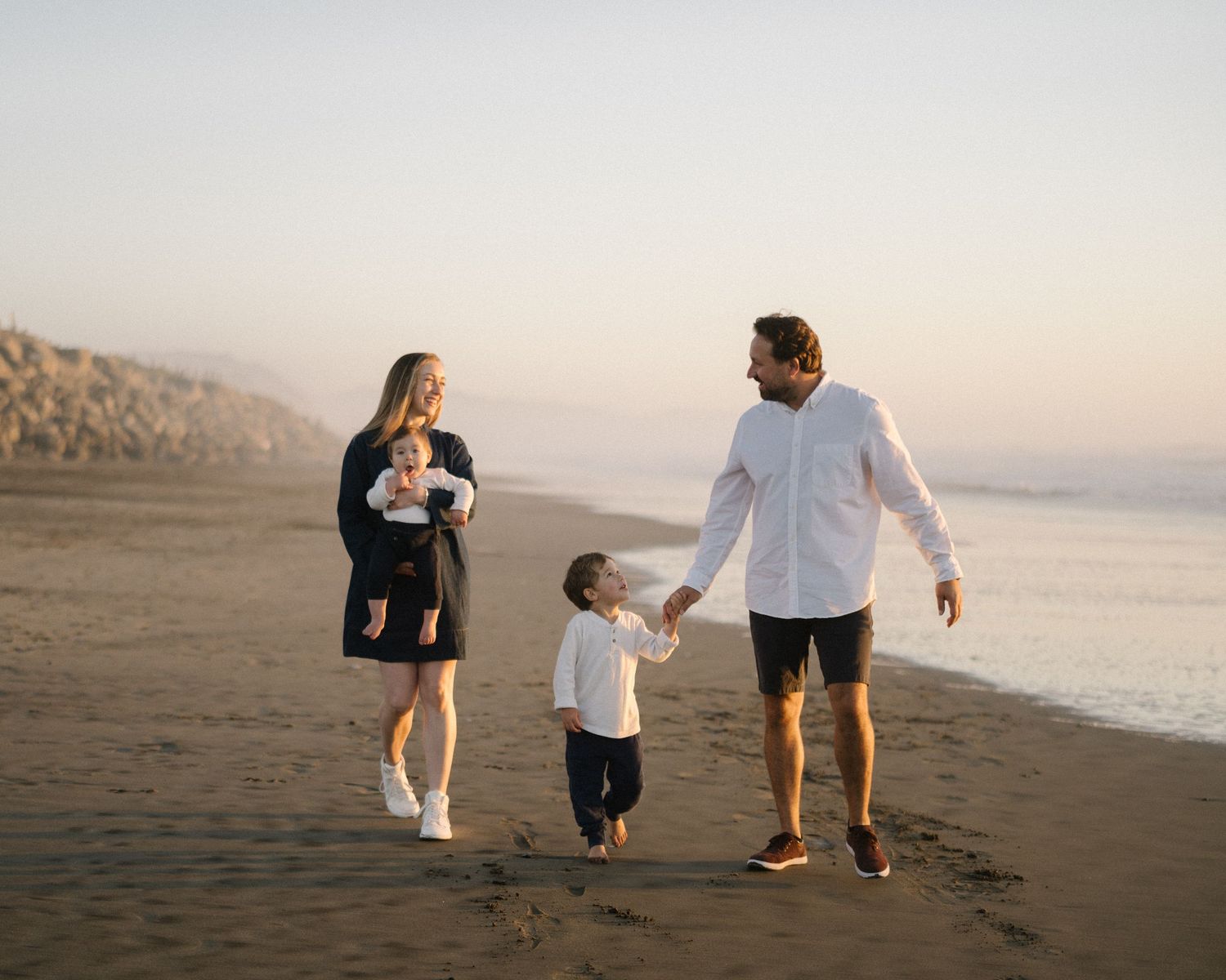 A family walks together along a misty beach at sunset holding hands on the shoreline.