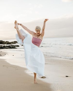 A person in a white flowing dress twirls gracefully on a serene beach at sunset, creating an ethereal silhouette.