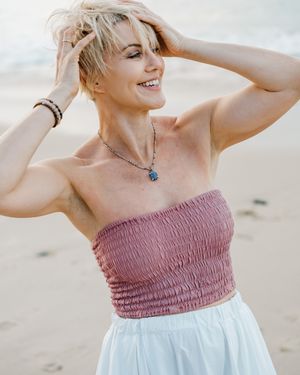 Person wearing a pink and white dress poses playfully on a sandy beach.
