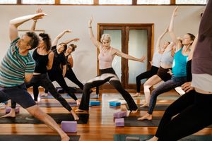 Yoga students practice various poses on colorful mats during a group fitness class in a sunlit studio.