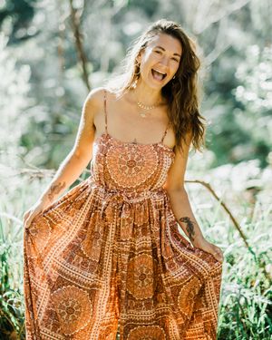 A joyful person wearing a brown patterned sundress twirls in a sunny outdoor setting with bokeh lighting effects.